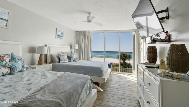 bedroom featuring a wall of windows, light hardwood / wood-style flooring, a textured ceiling, ceiling fan, and access to exterior