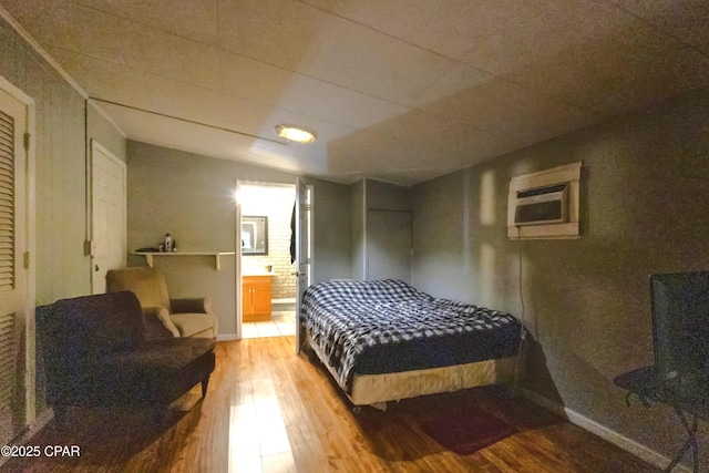 bedroom featuring hardwood / wood-style floors, a wall unit AC, and ensuite bath