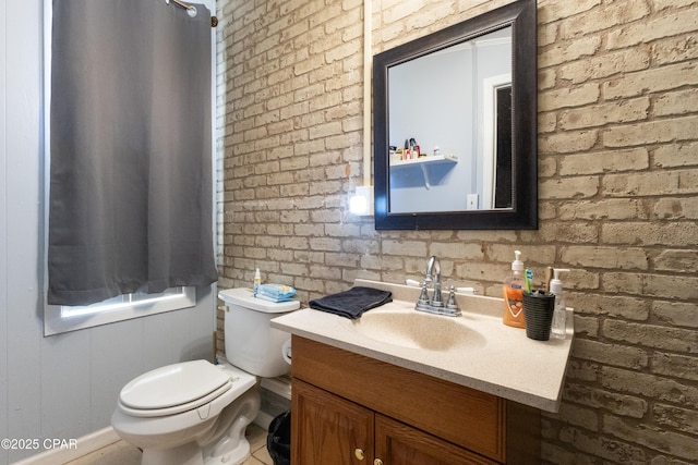 bathroom featuring vanity, toilet, and brick wall