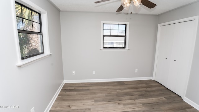 unfurnished bedroom with a closet, a textured ceiling, baseboards, and wood finished floors