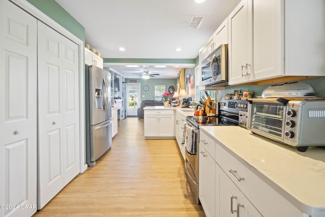 kitchen with kitchen peninsula, light wood-type flooring, stainless steel appliances, ceiling fan, and white cabinetry