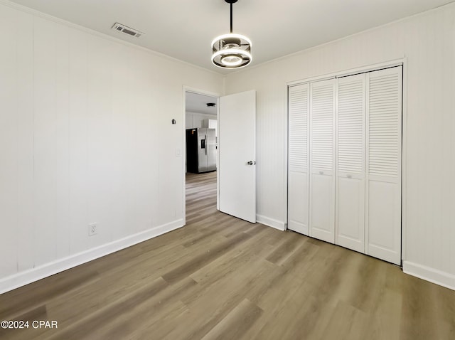 unfurnished bedroom featuring crown molding, a closet, stainless steel refrigerator with ice dispenser, and hardwood / wood-style flooring