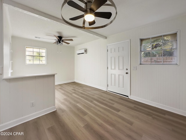 empty room featuring ceiling fan, a wall mounted AC, a textured ceiling, wooden walls, and hardwood / wood-style flooring