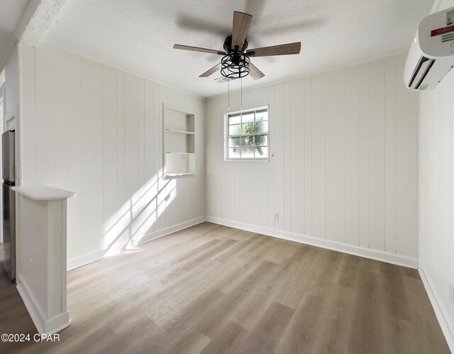 spare room featuring a wall mounted air conditioner, light wood-type flooring, ceiling fan, and wood walls