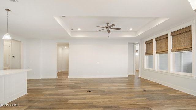 empty room with a raised ceiling, ceiling fan, and wood-type flooring