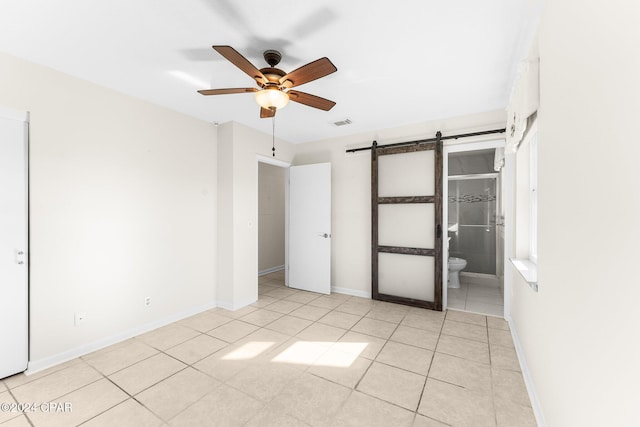 unfurnished bedroom with ceiling fan, a barn door, light tile patterned floors, and ensuite bath