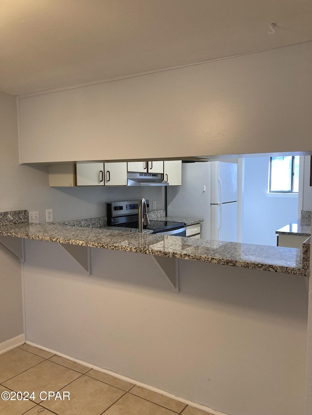 kitchen featuring light tile patterned floors, light stone counters, white refrigerator, electric stove, and white cabinets