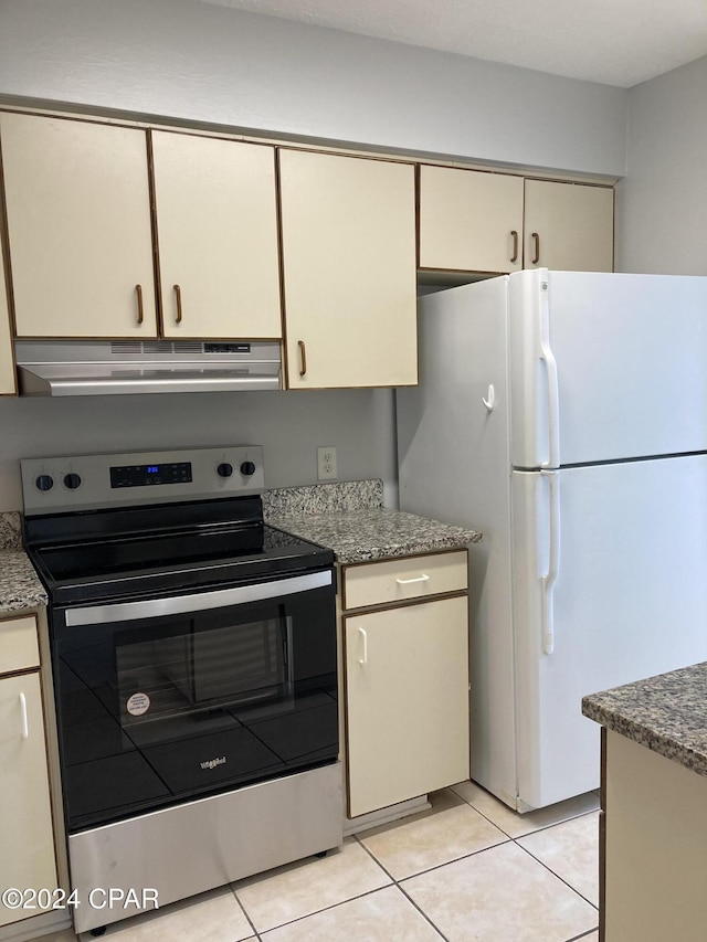 kitchen featuring light tile patterned flooring, dark stone counters, electric range, cream cabinetry, and white fridge