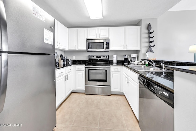 kitchen with sink, stainless steel appliances, light tile patterned floors, dark stone counters, and white cabinets