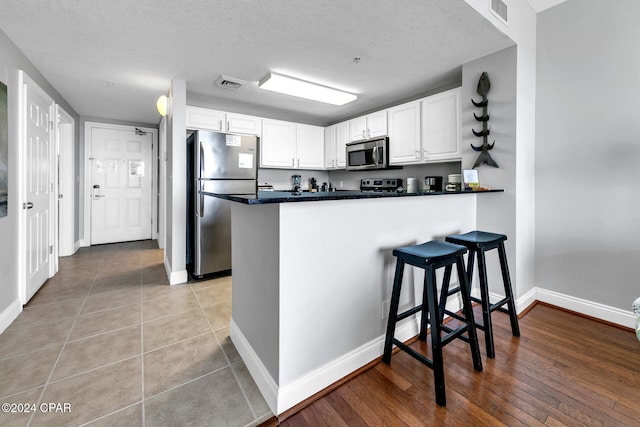 kitchen with kitchen peninsula, white cabinetry, light hardwood / wood-style floors, and appliances with stainless steel finishes