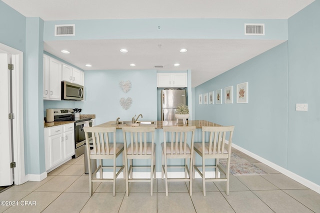 kitchen featuring stainless steel appliances, a breakfast bar area, visible vents, and white cabinetry