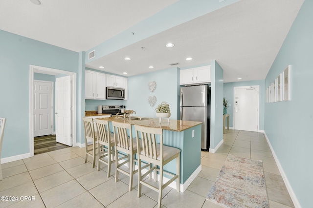 kitchen with white cabinets, a kitchen bar, a kitchen island with sink, stainless steel appliances, and light stone countertops