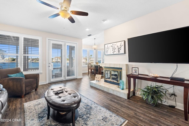 living room featuring a tile fireplace, dark wood-type flooring, and ceiling fan