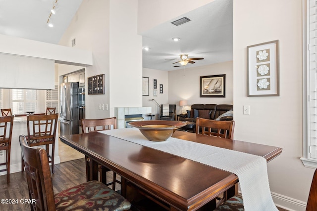 dining room with lofted ceiling, dark wood-type flooring, rail lighting, ceiling fan, and a fireplace