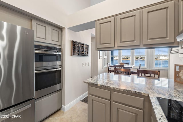 kitchen featuring light tile patterned floors, gray cabinetry, stainless steel appliances, a water view, and light stone counters