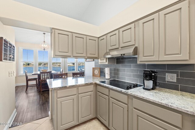 kitchen featuring light stone counters, black electric stovetop, kitchen peninsula, and backsplash