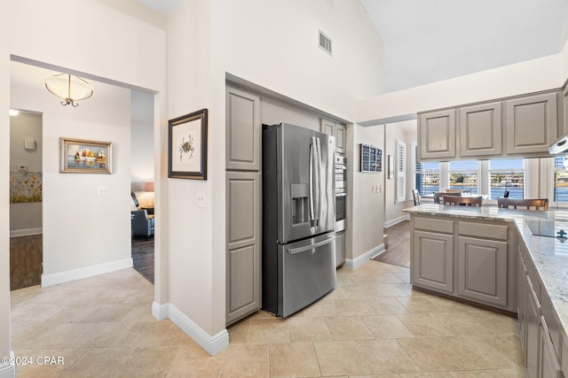 kitchen featuring gray cabinetry, hanging light fixtures, a towering ceiling, stainless steel refrigerator with ice dispenser, and light stone countertops