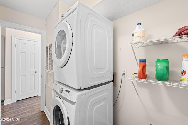 washroom with dark wood-type flooring, stacked washer and dryer, and a textured ceiling