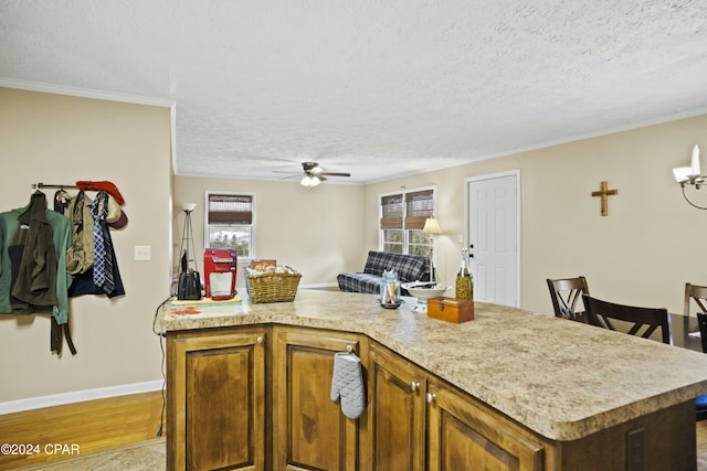 kitchen featuring a kitchen island, a textured ceiling, ceiling fan, and ornamental molding