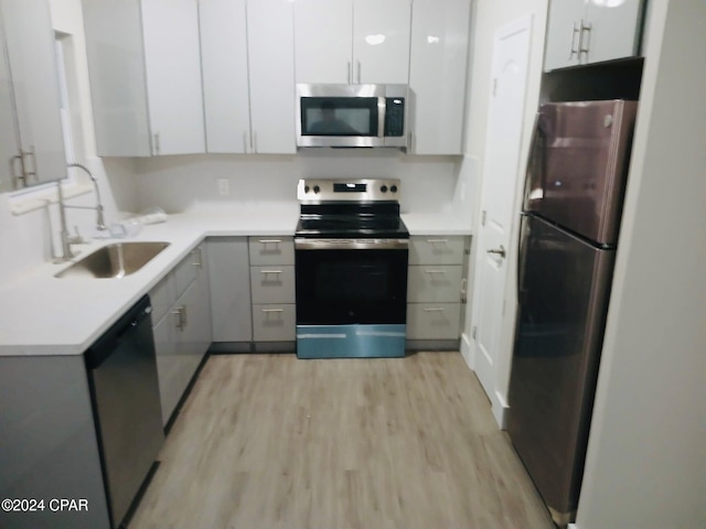 kitchen with gray cabinetry, sink, stainless steel appliances, white cabinets, and light wood-type flooring