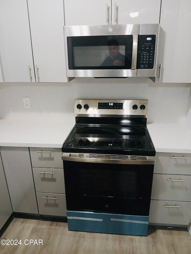 kitchen featuring white cabinets, light wood-type flooring, stainless steel appliances, and gray cabinetry