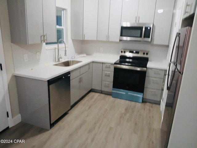 kitchen with appliances with stainless steel finishes, light wood-type flooring, gray cabinetry, sink, and white cabinetry