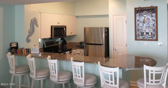 kitchen with white cabinetry, stainless steel refrigerator, range with electric cooktop, and dark stone counters