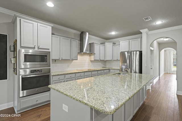 kitchen with a center island with sink, wall chimney exhaust hood, appliances with stainless steel finishes, and tasteful backsplash