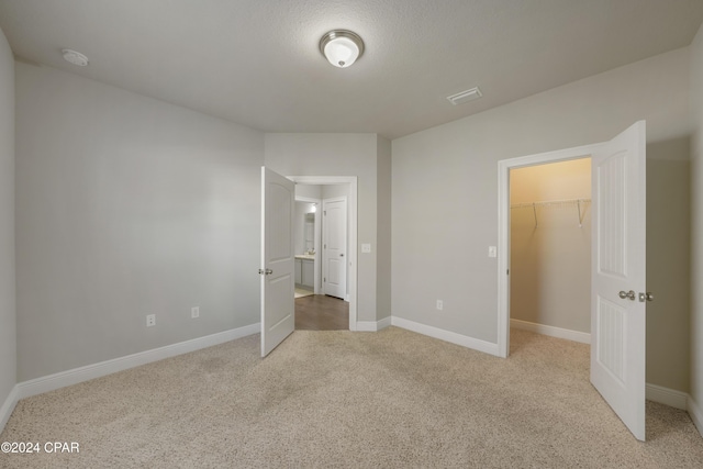 unfurnished bedroom with a walk in closet, light carpet, and a closet