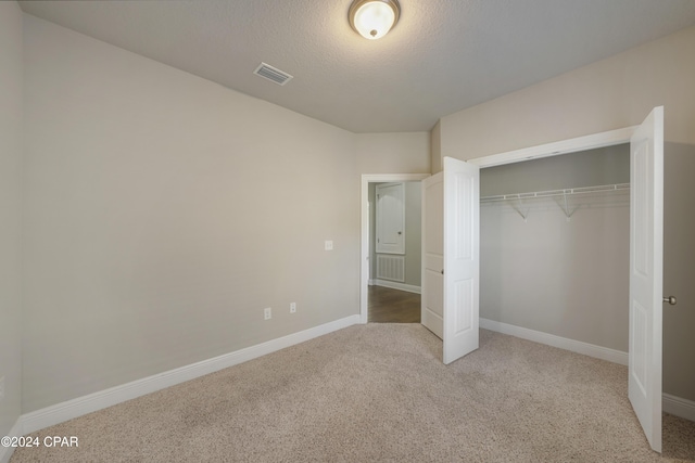 unfurnished bedroom with light carpet, a textured ceiling, and a closet