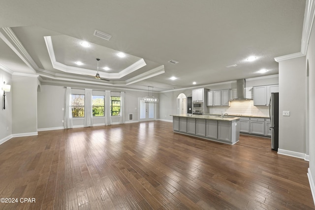 kitchen featuring gray cabinetry, wall chimney range hood, decorative backsplash, a kitchen island with sink, and ornamental molding