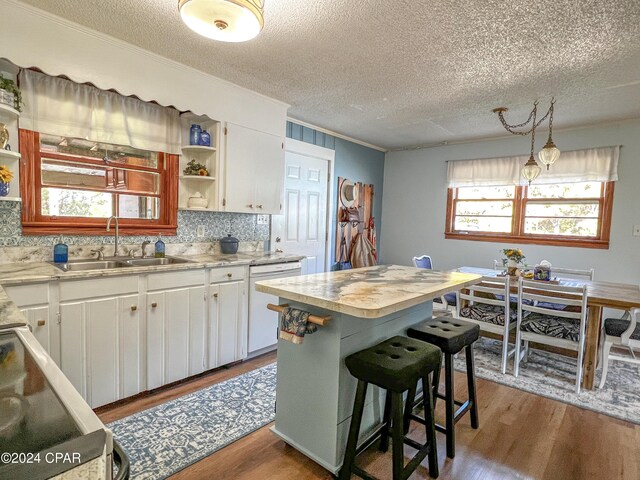 kitchen with a kitchen island, dishwasher, sink, white cabinets, and hanging light fixtures