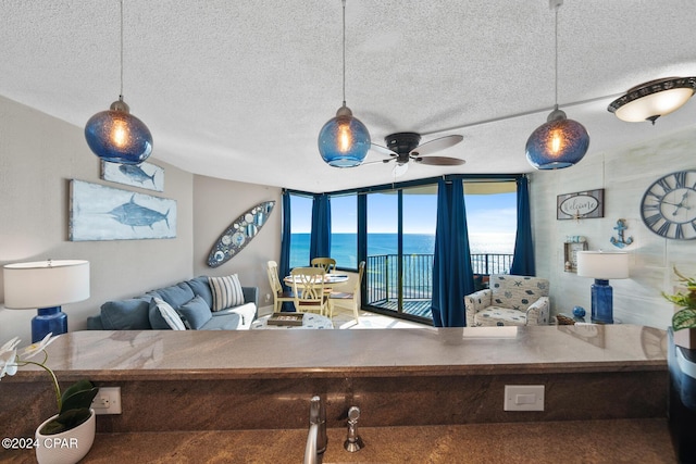 living room featuring ceiling fan, a textured ceiling, a wall of windows, and a water view