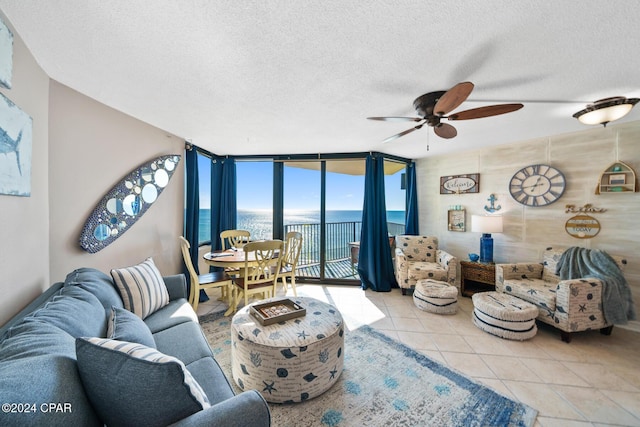 tiled living room featuring expansive windows, ceiling fan, a water view, and a textured ceiling