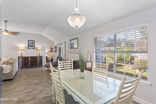 dining room featuring ceiling fan with notable chandelier, vaulted ceiling, and wood-type flooring