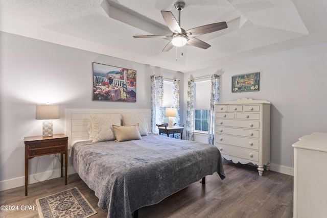 bedroom featuring a raised ceiling, ceiling fan, dark wood-type flooring, and a textured ceiling