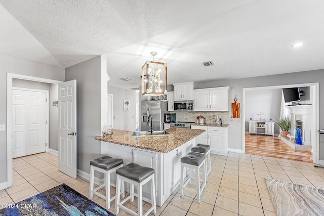 kitchen featuring light tile patterned flooring, white cabinets, a kitchen bar, kitchen peninsula, and stainless steel appliances