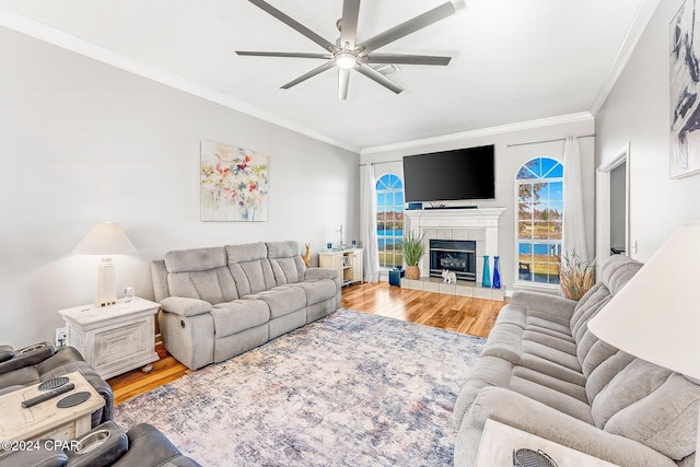 living room featuring hardwood / wood-style flooring, ceiling fan, crown molding, and a tile fireplace