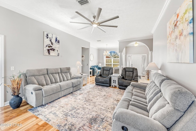 living room featuring ornate columns, ceiling fan with notable chandelier, hardwood / wood-style flooring, crown molding, and a textured ceiling