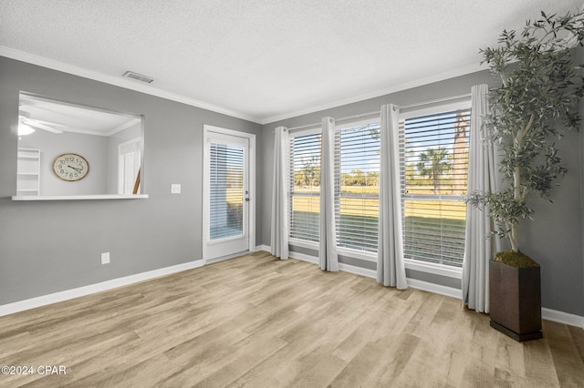 empty room featuring a textured ceiling, light wood finished floors, and crown molding