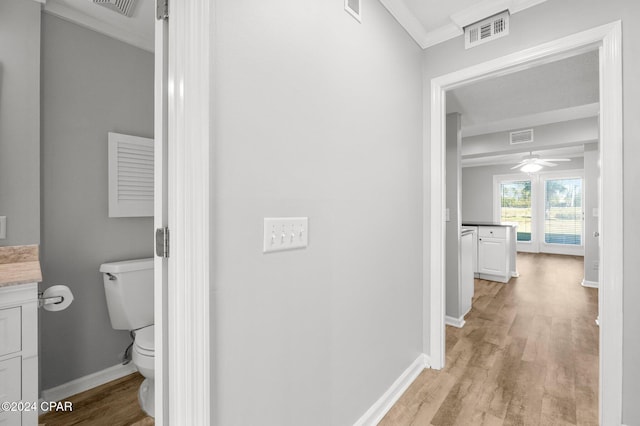 half bath with crown molding, visible vents, vanity, wood finished floors, and baseboards