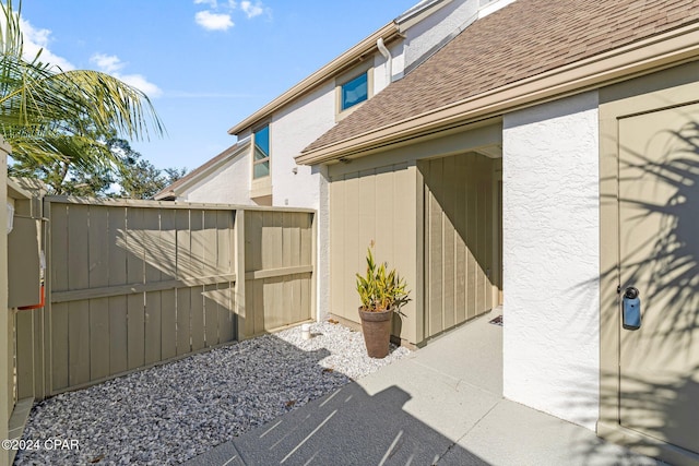 exterior space featuring stucco siding, fence, and roof with shingles