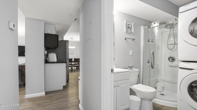 bathroom featuring vanity, a shower, hardwood / wood-style floors, toilet, and stacked washer / drying machine