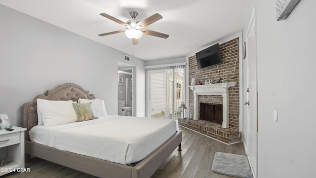 bedroom with hardwood / wood-style flooring, ceiling fan, ensuite bathroom, and a brick fireplace