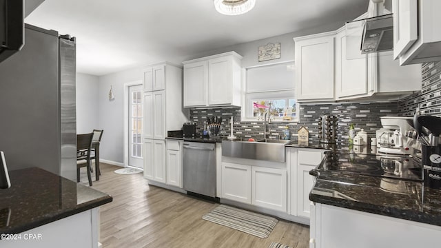 kitchen with dark stone counters, white cabinets, sink, light wood-type flooring, and appliances with stainless steel finishes