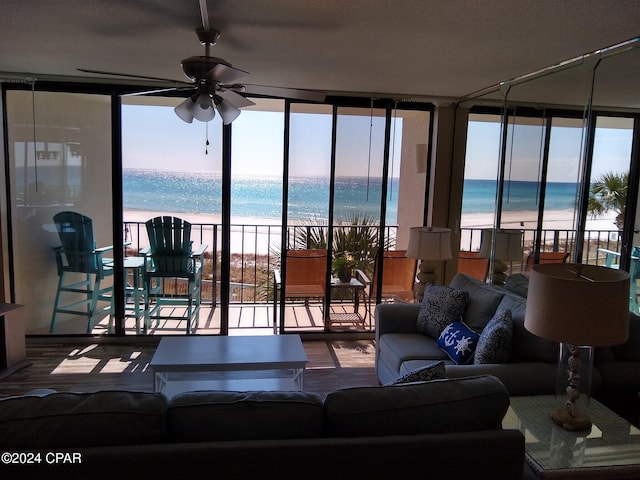 living room featuring expansive windows, ceiling fan, a view of the beach, wood-type flooring, and a water view