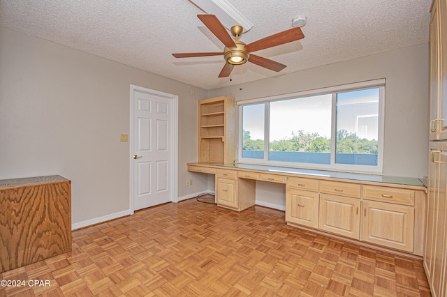 unfurnished office featuring built in desk, a textured ceiling, ceiling fan, and light parquet floors