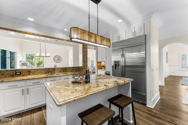 kitchen with pendant lighting, sink, white cabinetry, dark wood-type flooring, and stainless steel built in refrigerator