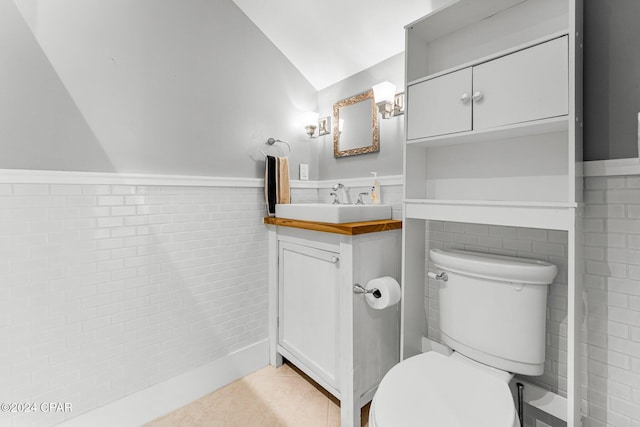 bathroom featuring toilet, lofted ceiling, tile patterned floors, tile walls, and vanity