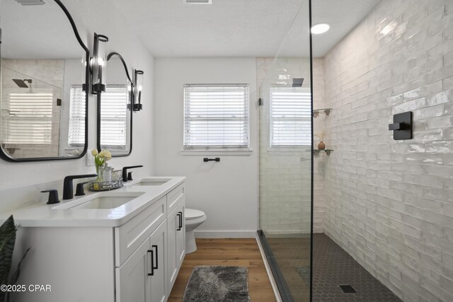 bathroom with toilet, tiled shower, a sink, and wood finished floors